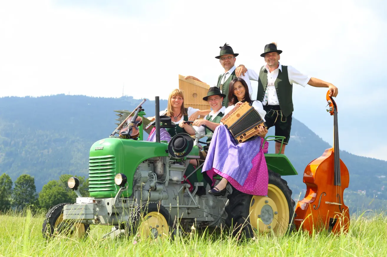 A group of musicians dressed in traditional attire are posing on a green tractor with musical instruments in a grassy field.