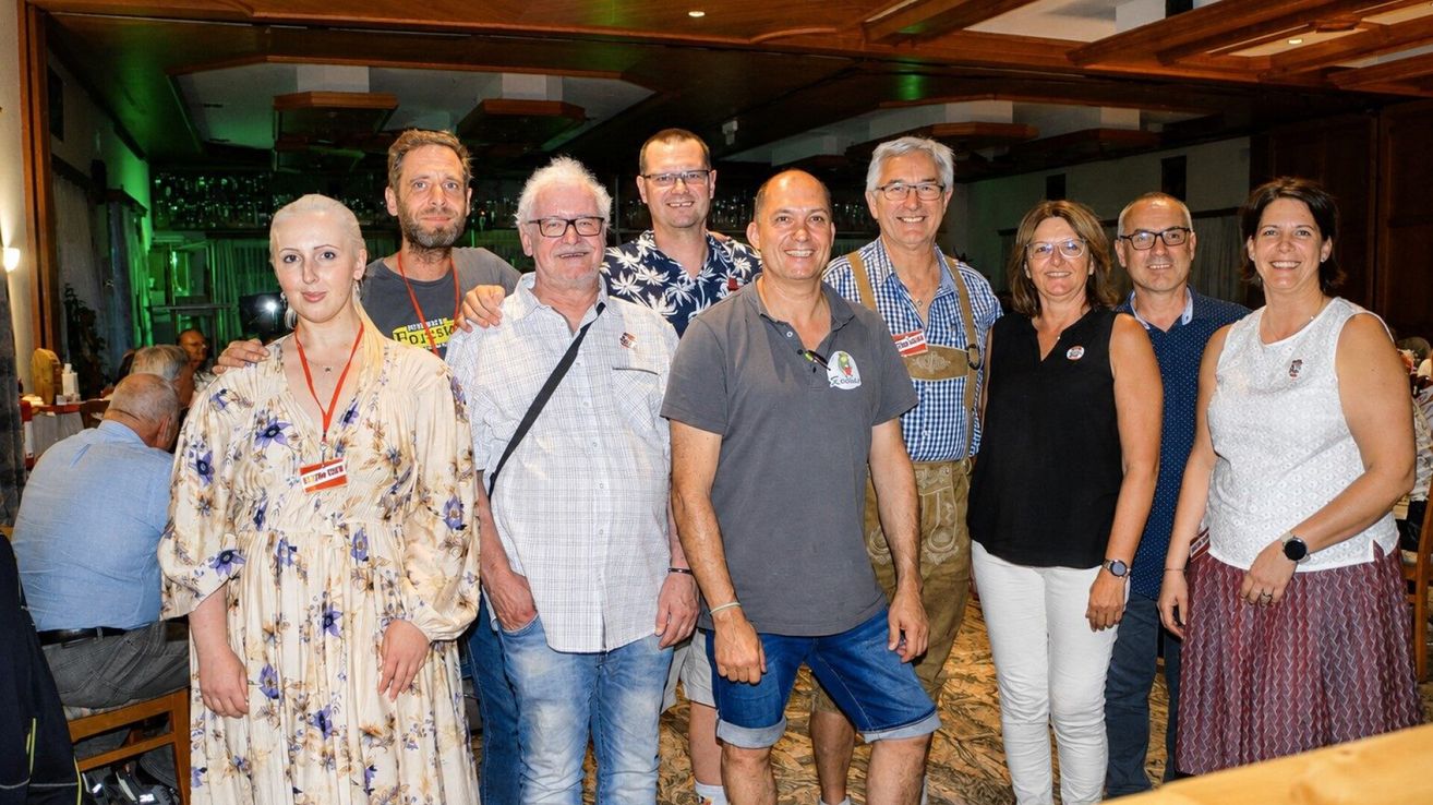 A group of people standing together, smiling for a photo. They are dressed casually and appear to be at a social gathering.