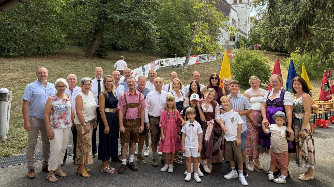 Eine Gruppe von Menschen, einschließlich Erwachsener und Kindern, posiert für ein Foto vor einer Kirche. Einige tragen traditionelle Kleidung.