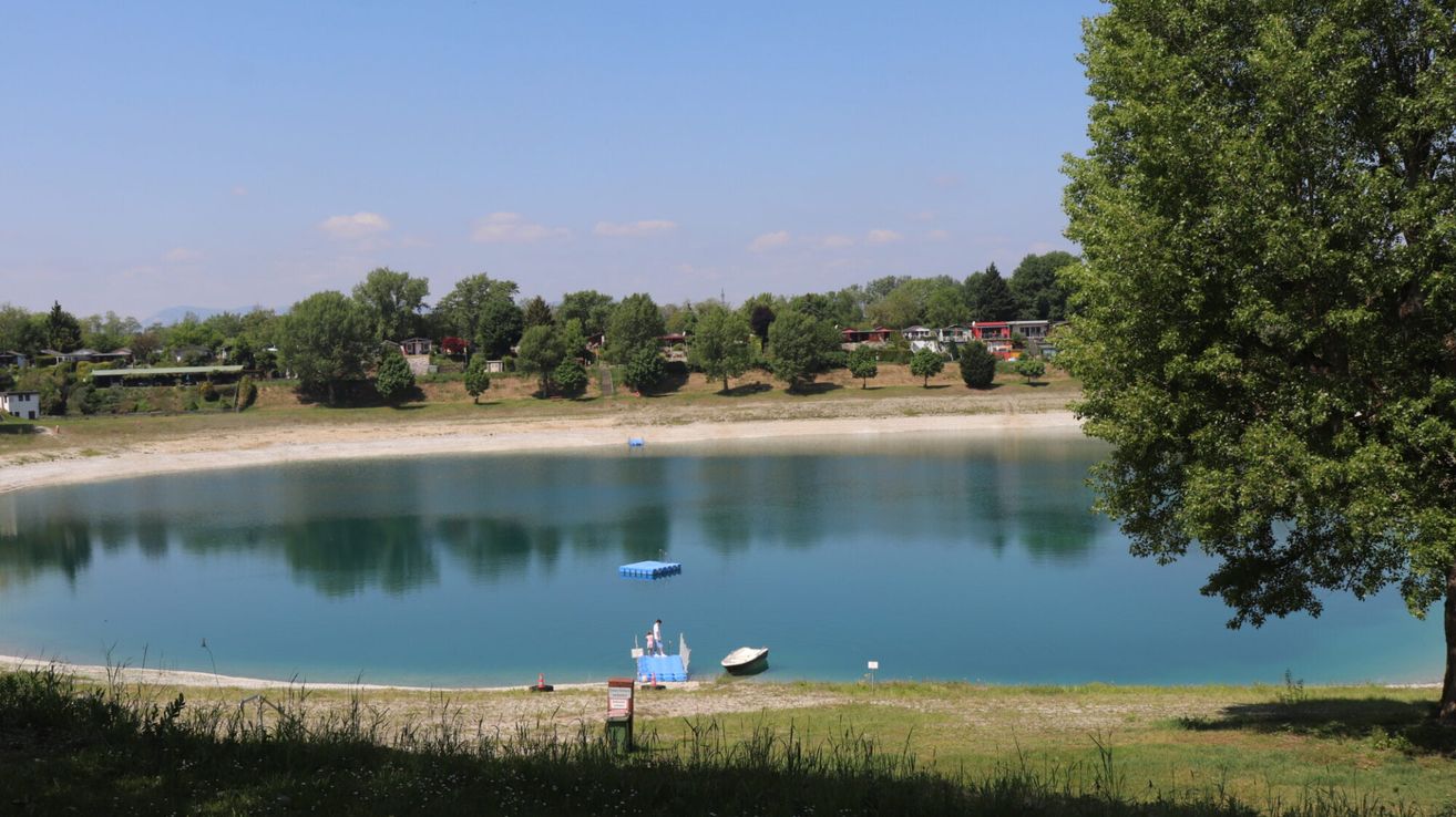 A serene lake with a small boat and a floating platform, surrounded by trees and a clear blue sky.