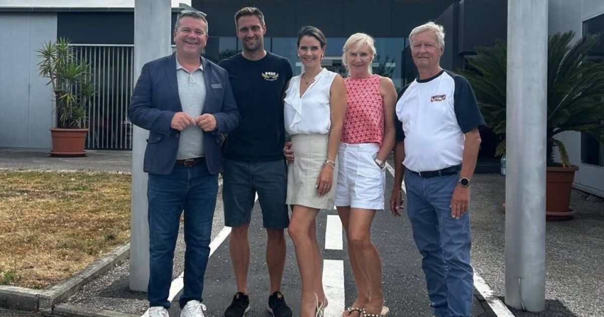 Fünf Menschen stehen in einem Parkplatz vor einem Gebäude. Drei Männer und zwei Frauen lächeln und posieren für ein Foto.