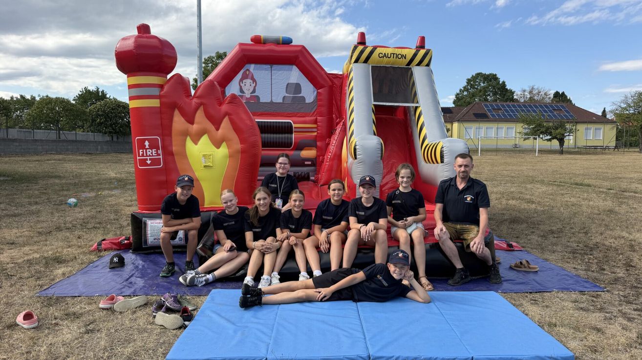 A group of children and adults pose for a photo in front of a fire truck bouncy castle.