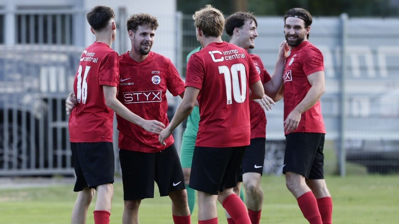 Eine Gruppe von Fußballspielern in roten Trikots feiert auf einem Feld, wobei ein Spieler das Trikot mit der Nummer 10 trägt.
