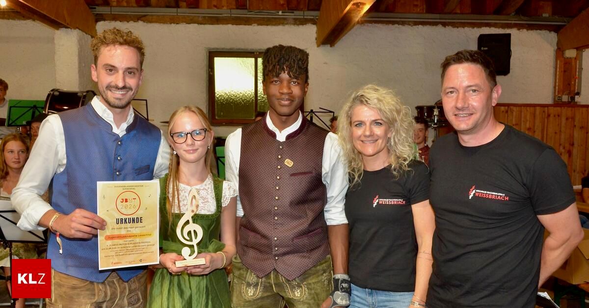 Eine Gruppe von Menschen steht zusammen und lächelt für ein Foto. Eine Frau hält eine Trophäe und ein Mann ein Zertifikat. Sie sind alle in traditioneller Kleidung gekleidet.