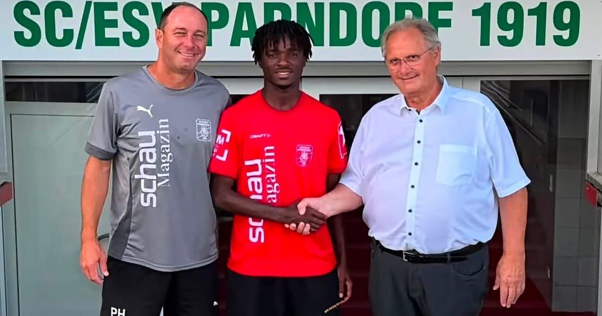 Drei Männer stehen zusammen, einer in einem grauen Shirt, einer in einem roten Shirt und einer in einem blauen Shirt, lächeln und schütteln Hände.