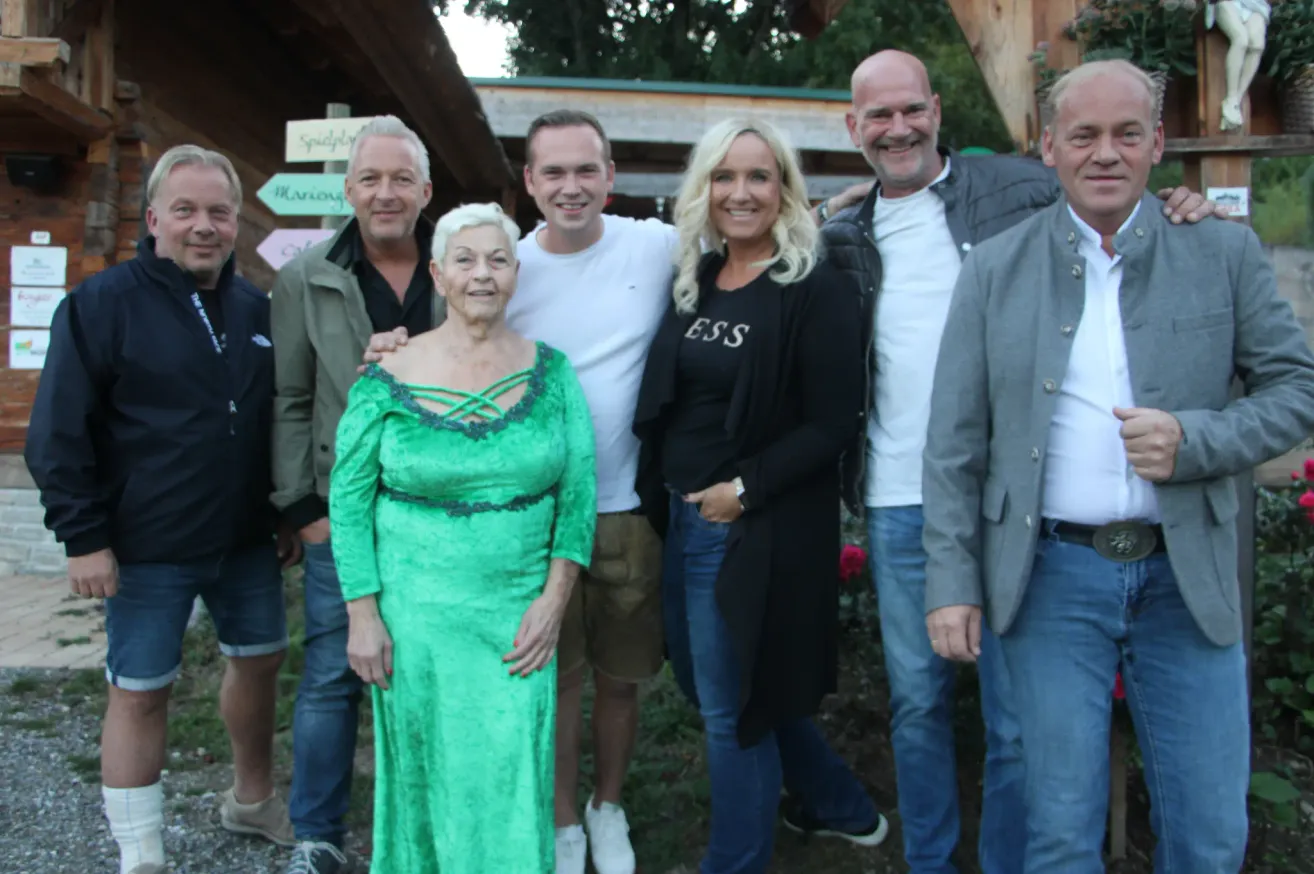 Eine Gruppe von Menschen, darunter eine Frau in einem grünen Kleid, posiert für ein Foto im Garten.