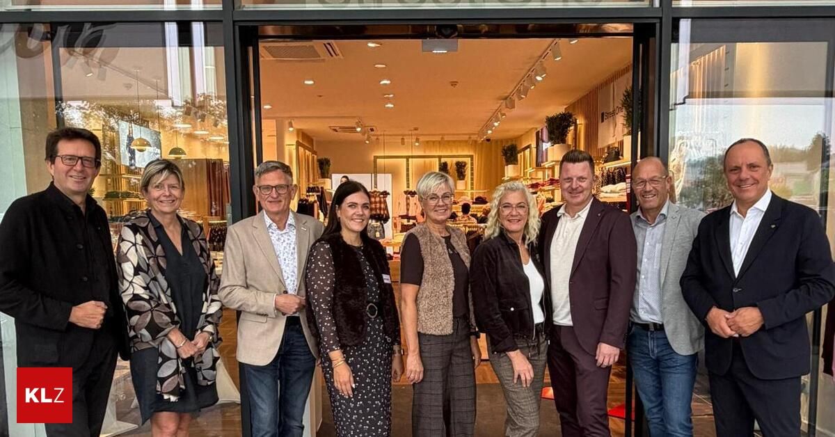 Eine Gruppe von Menschen steht vor einem Geschäft, lächelt und posiert für ein Foto. Sie sind alle festlich gekleidet.