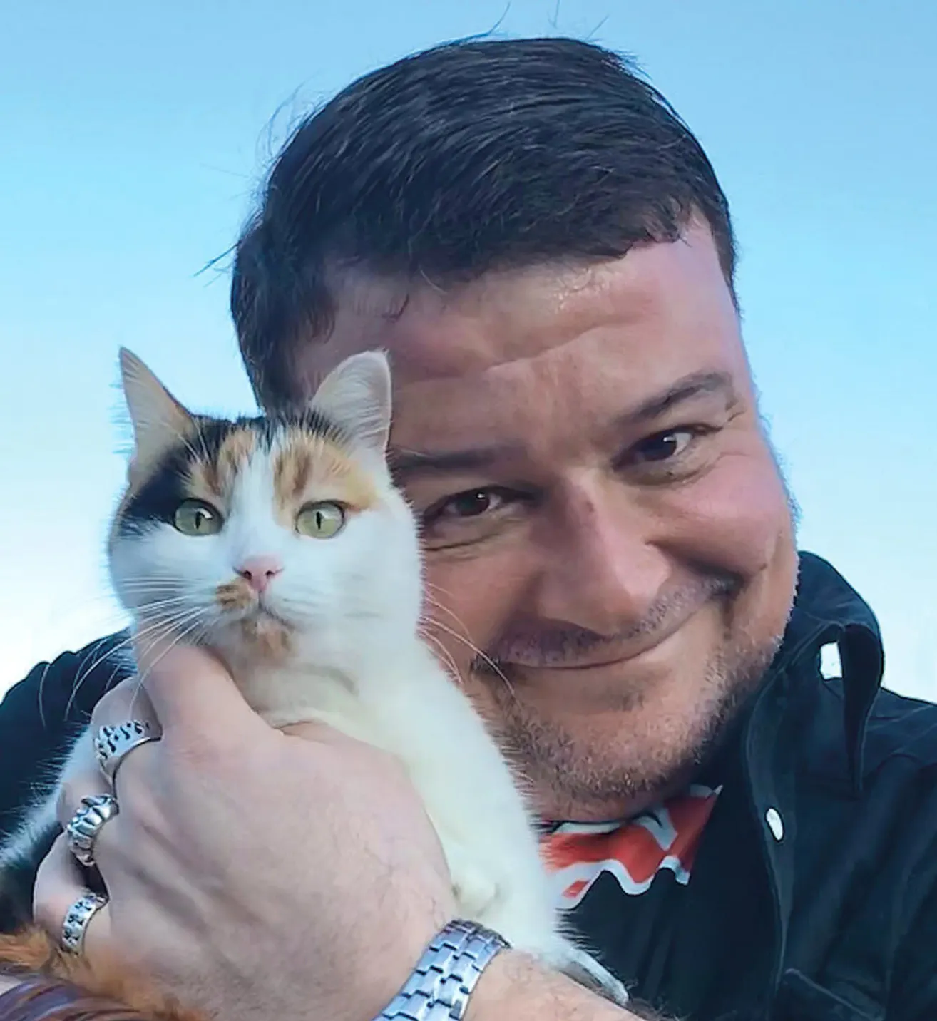 Ein Mann mit Bart hält eine getigerte Katze in den Armen und lächelt.