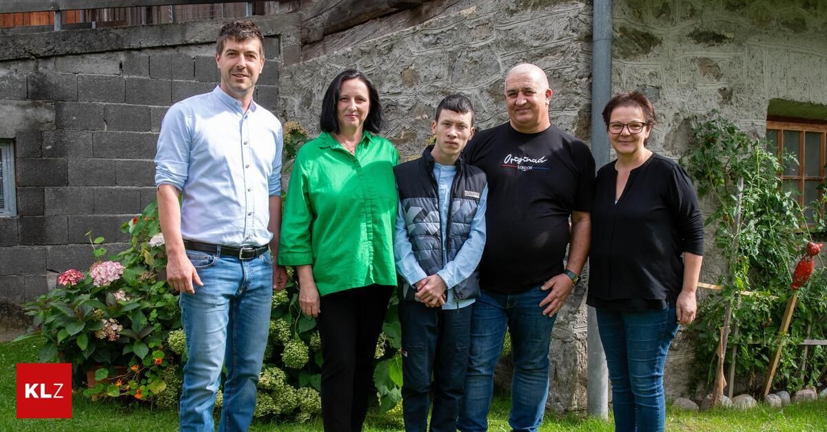 Fünf Personen stehen vor einer Steinmauer. Der Mann links trägt ein weißes Hemd und Jeans. Die Frau in der Mitte trägt ein grünes Hemd. Der Mann in der Mitte trägt eine Jacke. Der Mann rechts trägt ein schwarzes Hemd. Die Frau rechts trägt eine Brille.