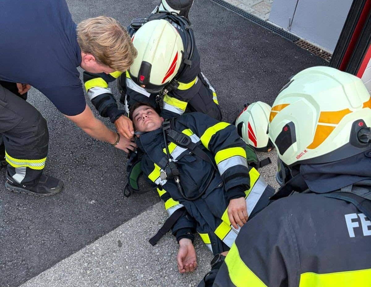Ein Feuerwehrmann liegt auf dem Boden und wird von zwei anderen Feuerwehrleuten in Uniform und Helmen betreut.