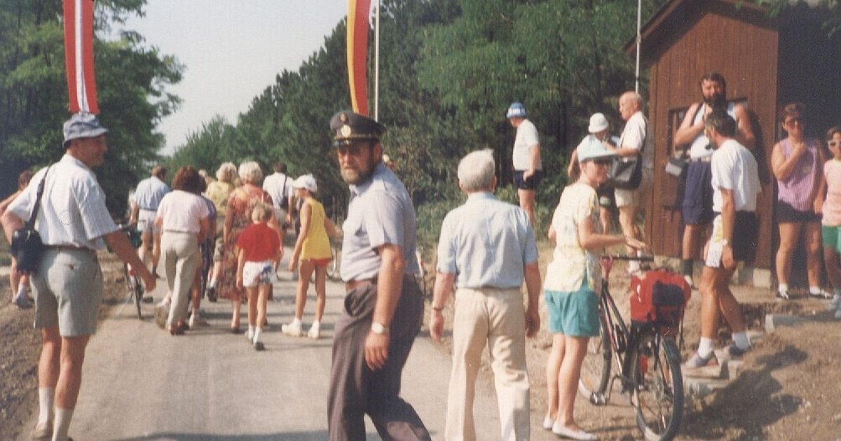 Eine Gruppe von Menschen, die auf einer Straße gehen, angeführt von einem Mann in Uniform. Ein Fahrrad ist am Straßenrand geparkt.