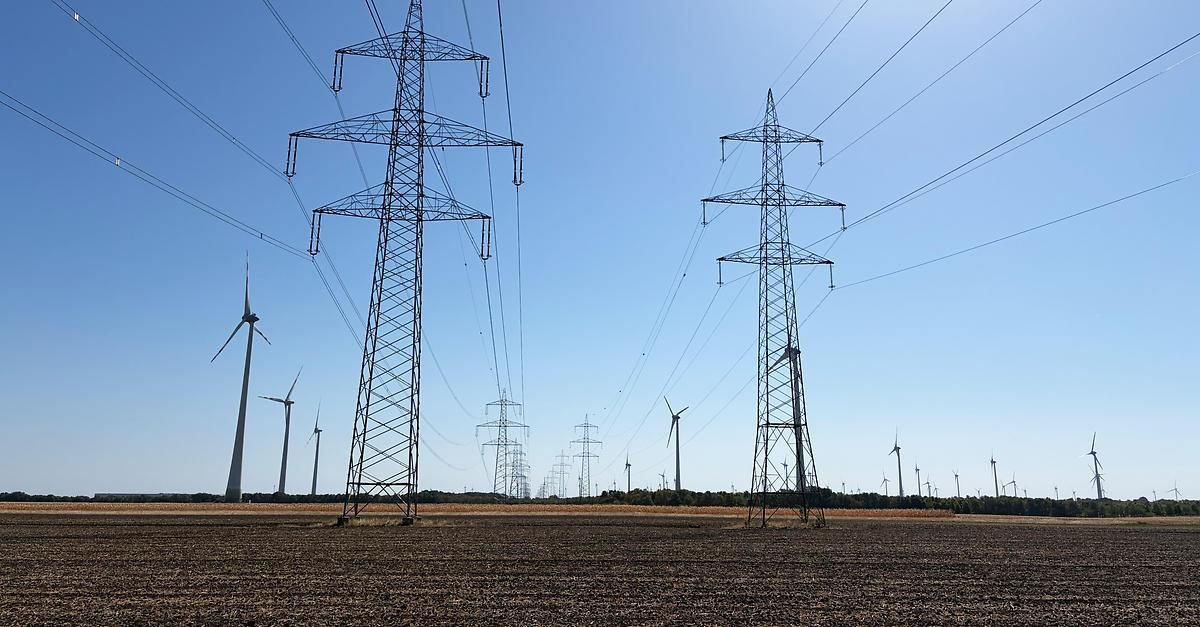 Ein Feld mit mehreren Windturbinen und Stromleitungsmasten unter einem klaren blauen Himmel.