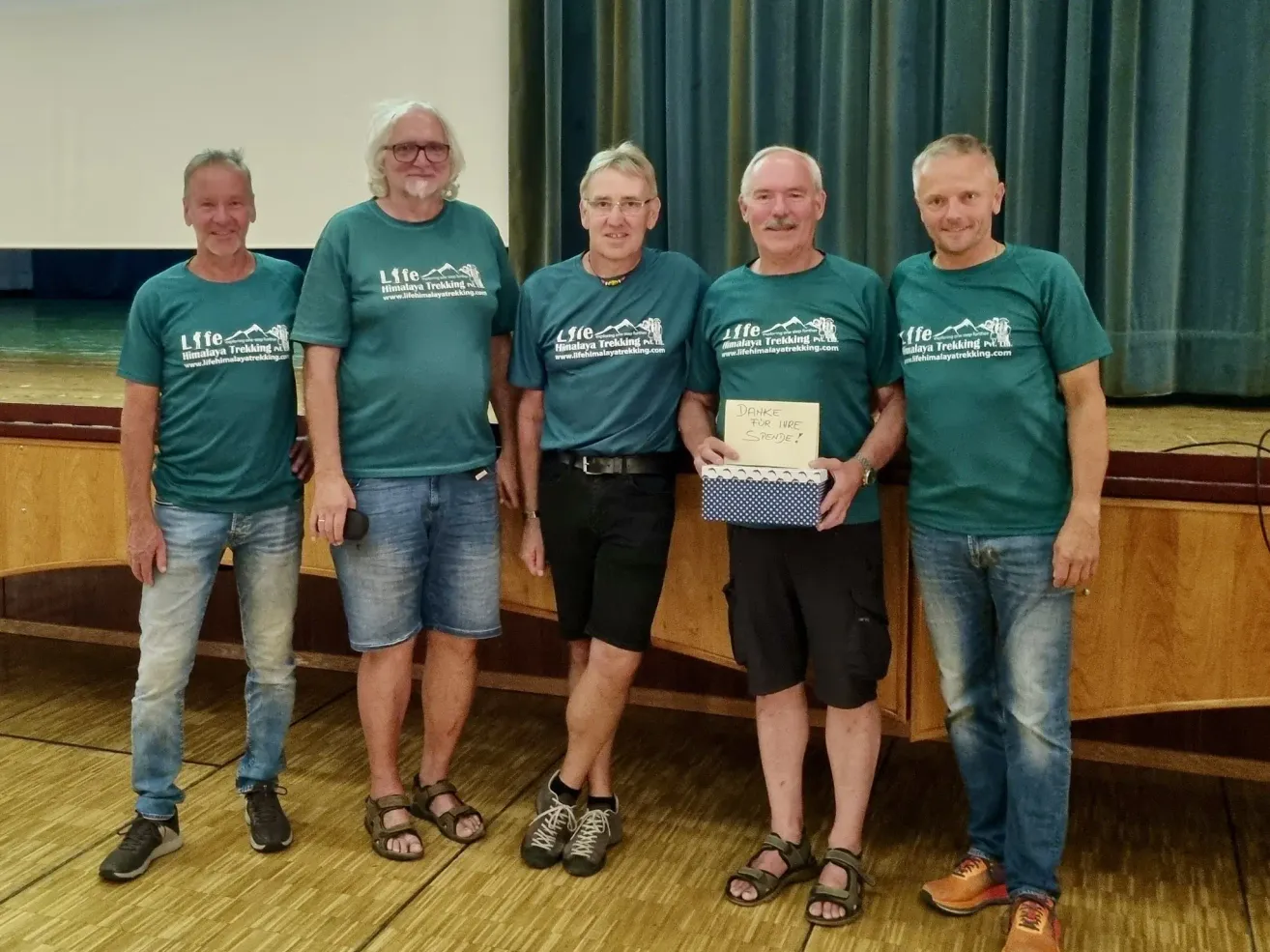 Five men in matching green t-shirts stand together, one holding a box and a note that says Danke for IWR.