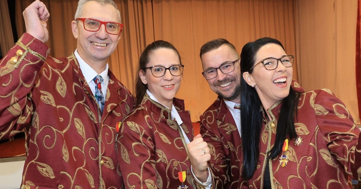 Vier Personen in passenden, burgunderroten Uniformen mit goldenen Akzenten lächeln und posieren für ein Foto. Die Frau in der Mitte hat eine Medaille auf ihrer linken Schulter.