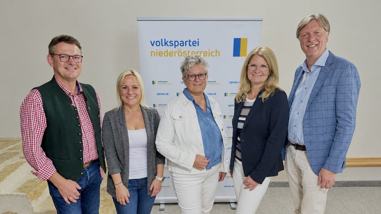 Five individuals stand in front of a banner with the text 'volkspartei niederösterreich'. The woman on the left wears a gray jacket, the middle woman has glasses and a white jacket, and the woman on the right wears a blue blazer. The two men on the sides wear casual attire.