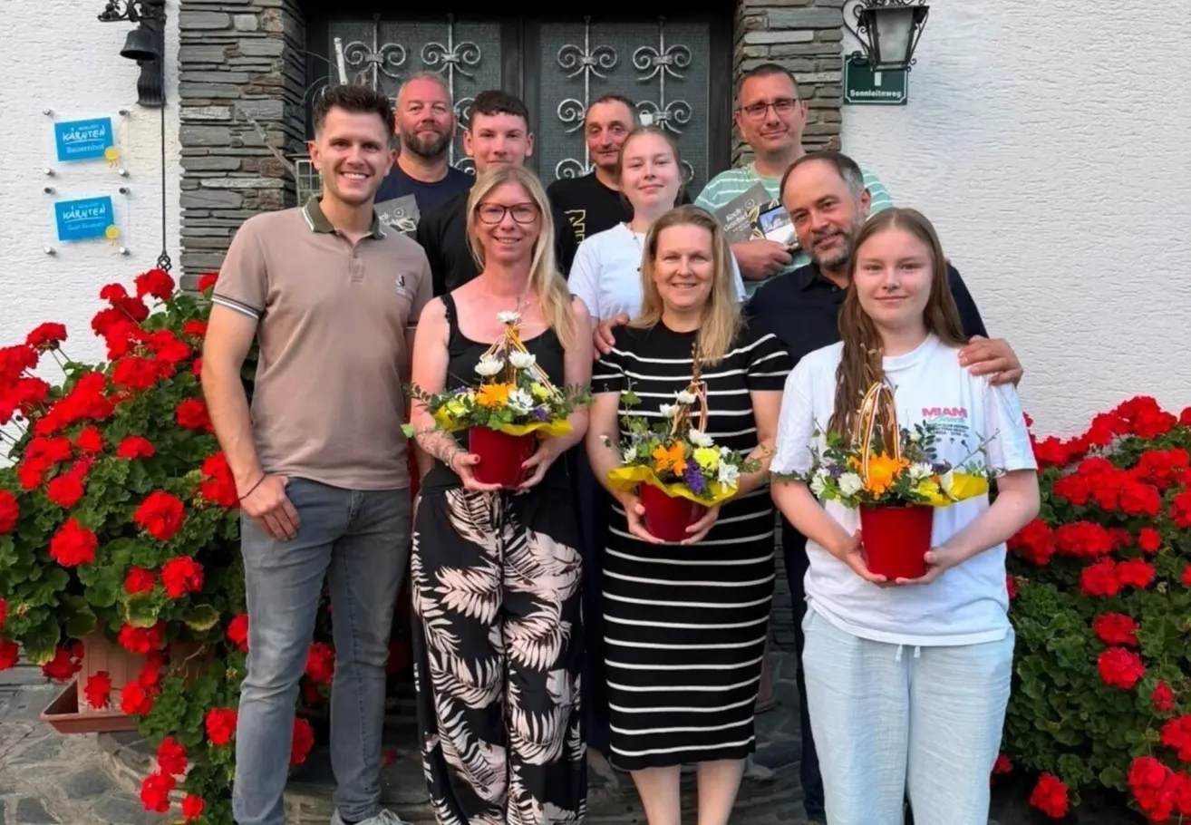 Eine Gruppe von Menschen, darunter Frauen mit Blumenkörben, steht vor einem Gebäude.