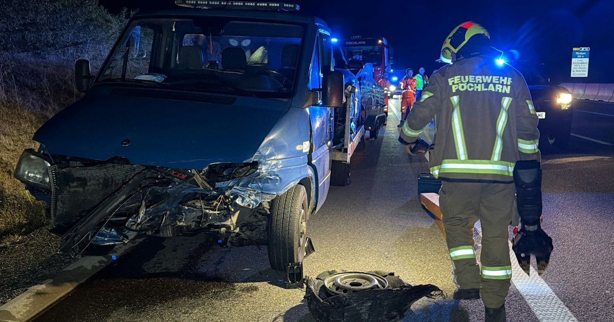 A firefighter in uniform stands beside a wrecked blue van on the side of the road at night.