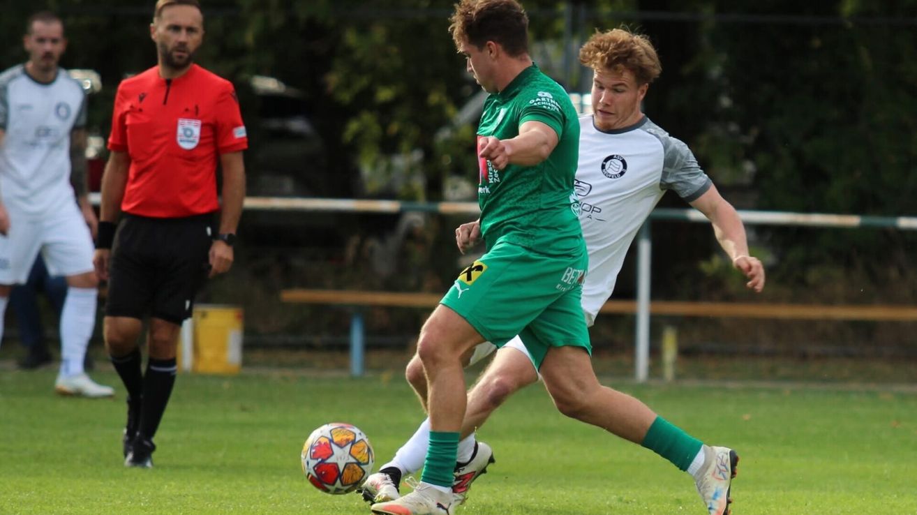 Two soccer players in green and white jerseys are competing for the ball on a grassy field.