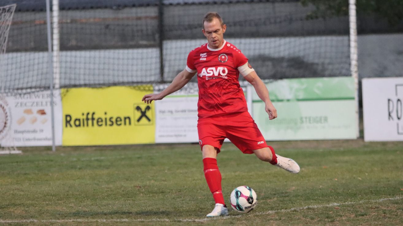 Ein Fußballspieler in einem roten Trikot tritt einen Ball auf dem Feld.
