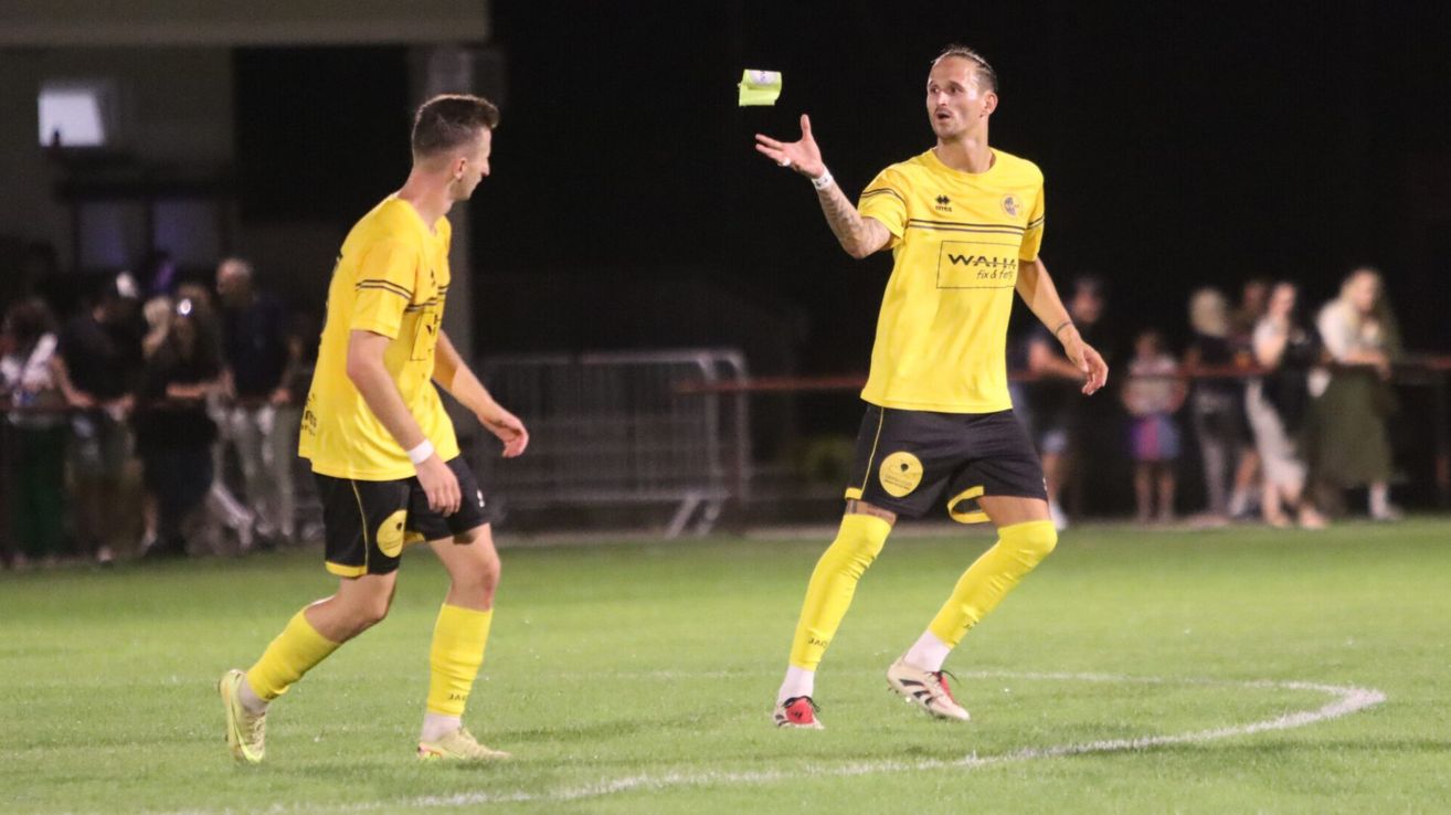 Zwei Fußballspieler in gelben Trikots auf einem Feld bei Nacht, einer hält eine gelbe Karte.