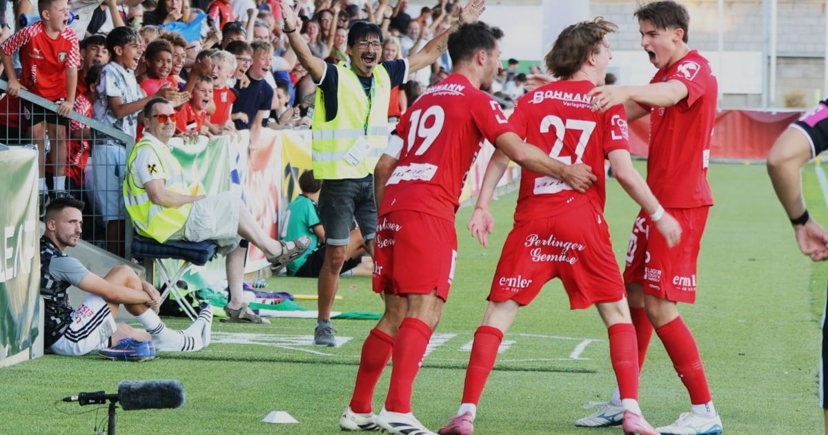 Fußballspieler in roten Trikots feiern ein Tor auf dem Feld, während die Menge im Hintergrund jubelt.