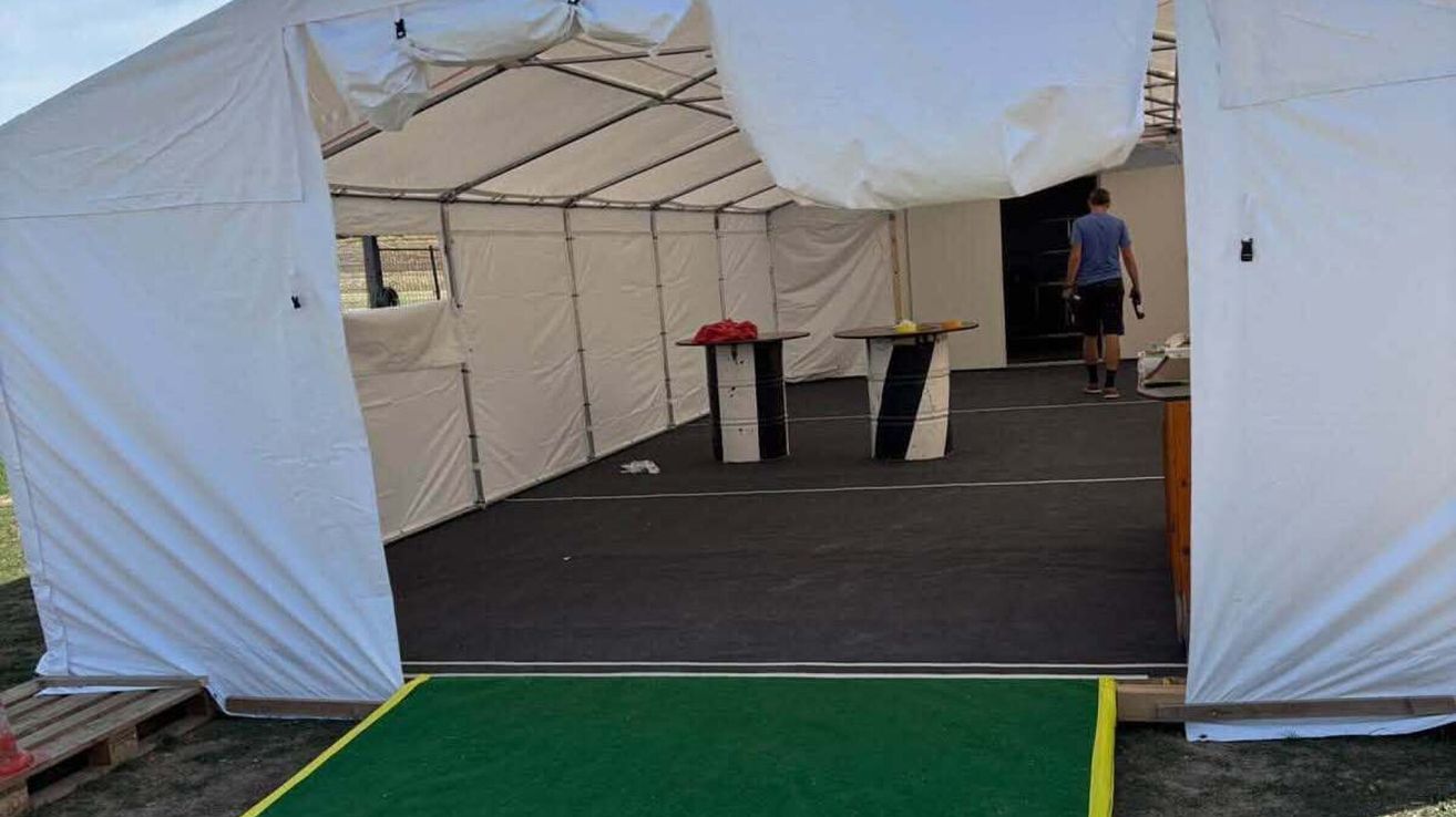 An empty tent with two tables, one with a red cloth on top, and a person walking in the background.
