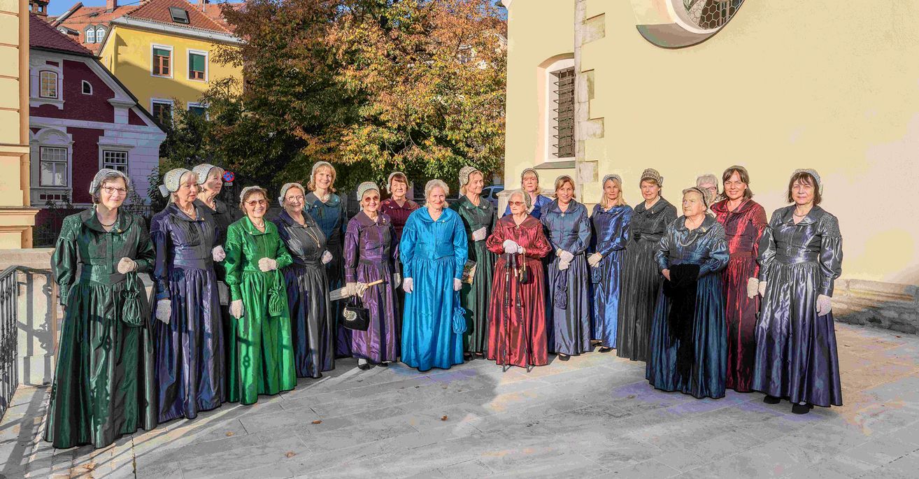 Eine Gruppe von Frauen in Vintage-Kleidung, die vor einem Gebäude stehen. Sie lächeln und scheinen für ein Foto zu posieren.