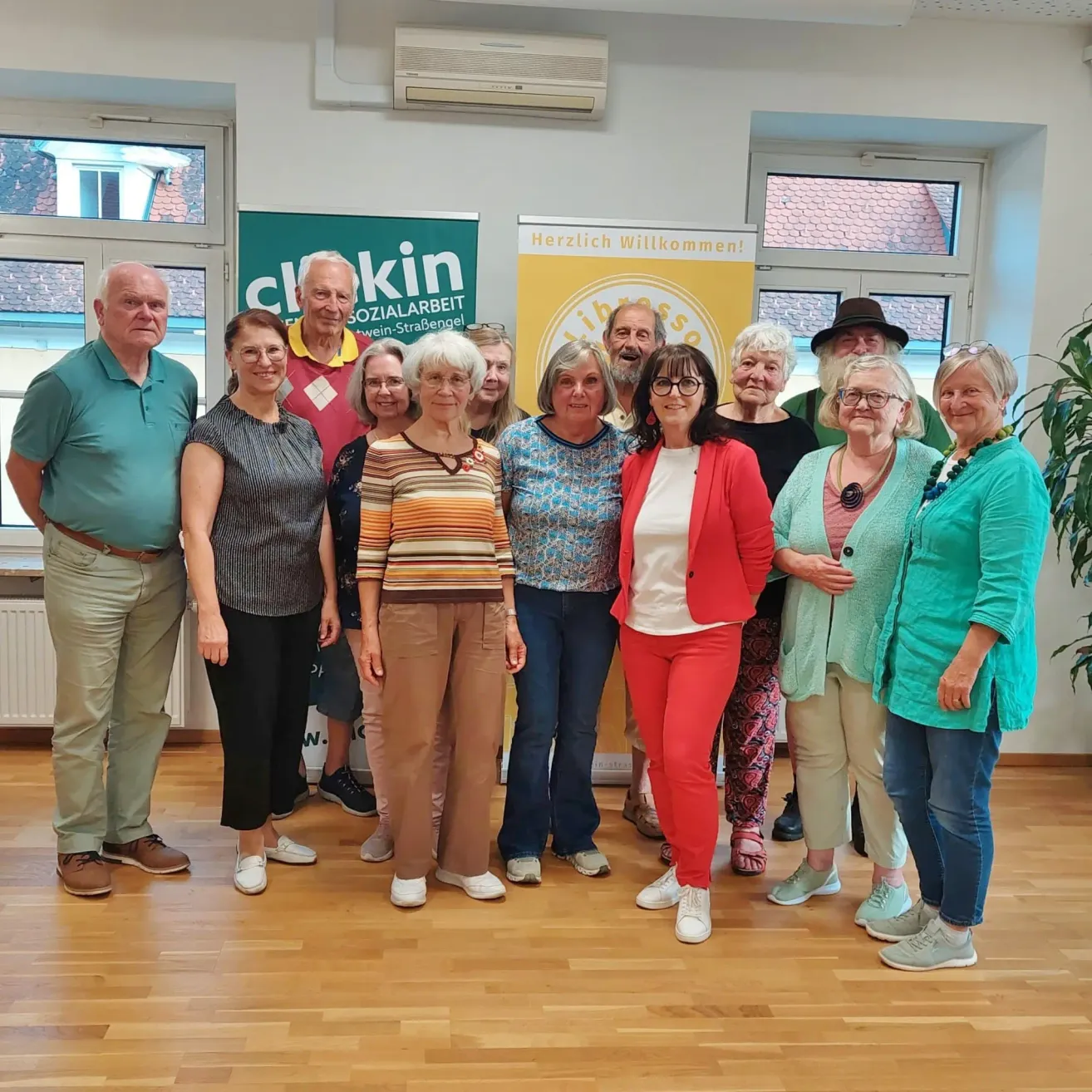 A group of people are posing for a photo in a room with wooden floors and banners on the wall.