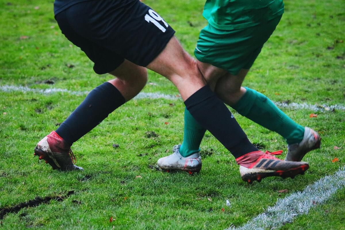 Zwei Fußballspieler, einer in Schwarz und einer in Grün, sind auf einem Rasenfeld in einen körperlichen Kampf verwickelt.