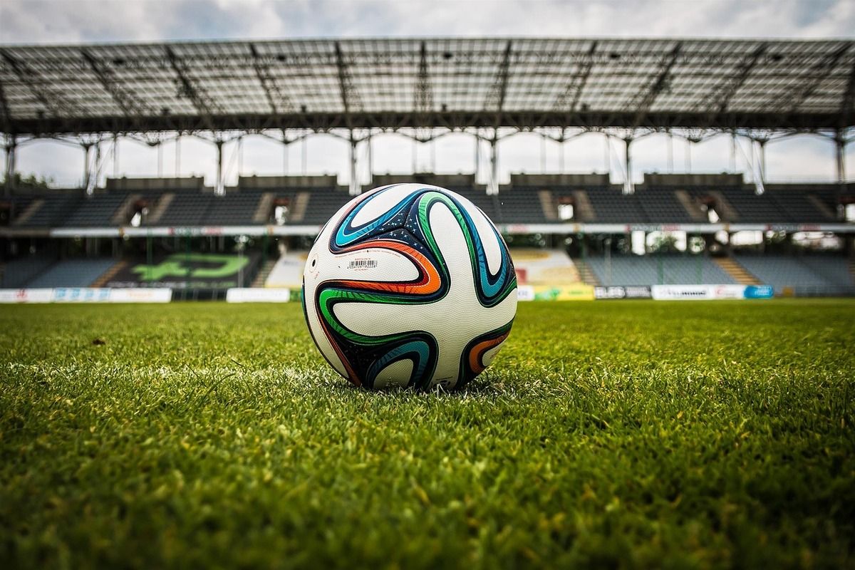 Ein Fußball mit leuchtenden Farben liegt auf einem grünen Feld in einem leeren Stadion.