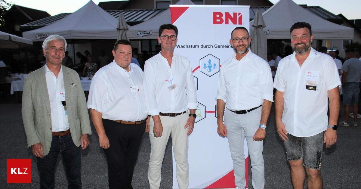 Fünf Männer in weißen Hemden und Gürteln stehen vor einem Banner mit dem Text 'BNI Wachstum durch Gemains'. Sie sind wahrscheinlich bei einer Veranstaltung.