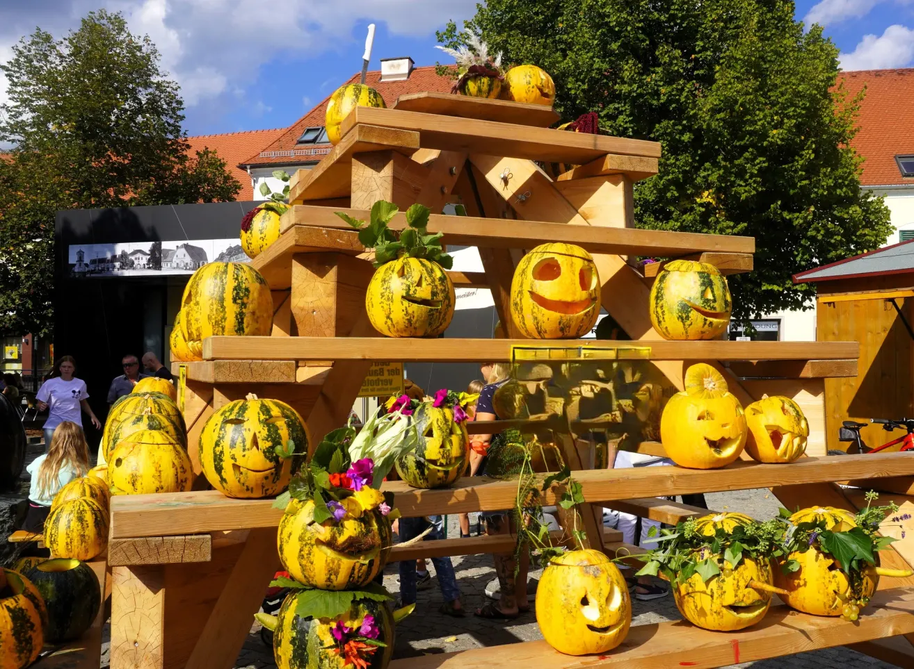 Eine hölzerne Pyramide aus Kürbissen mit geschnitzten Gesichtern, ausgestellt im Freien.