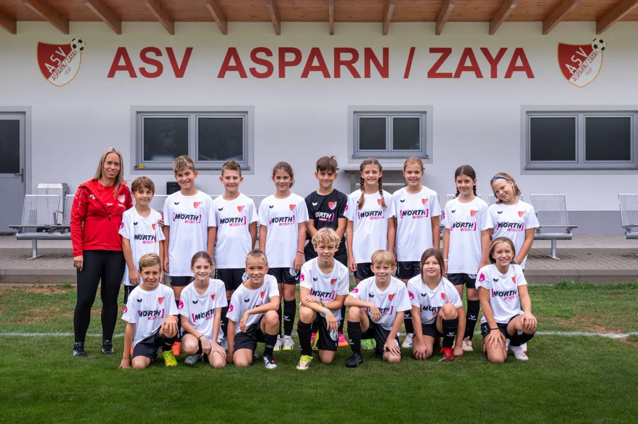 A group of young soccer players in white jerseys with the word 'NORTH' on them are posing for a photo in front of a building.
