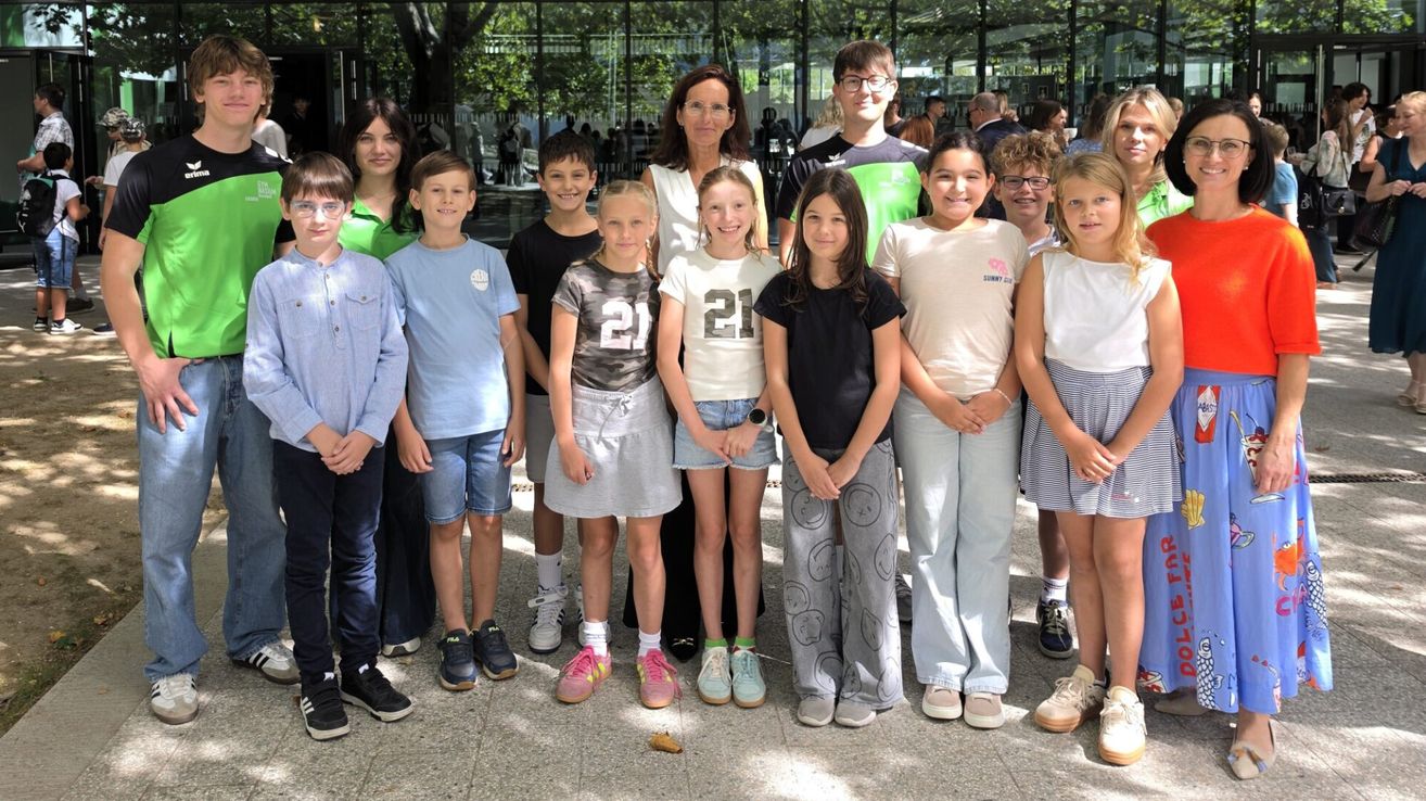 A group of children and adults standing together for a photo, with a woman in the middle wearing glasses and a white top.