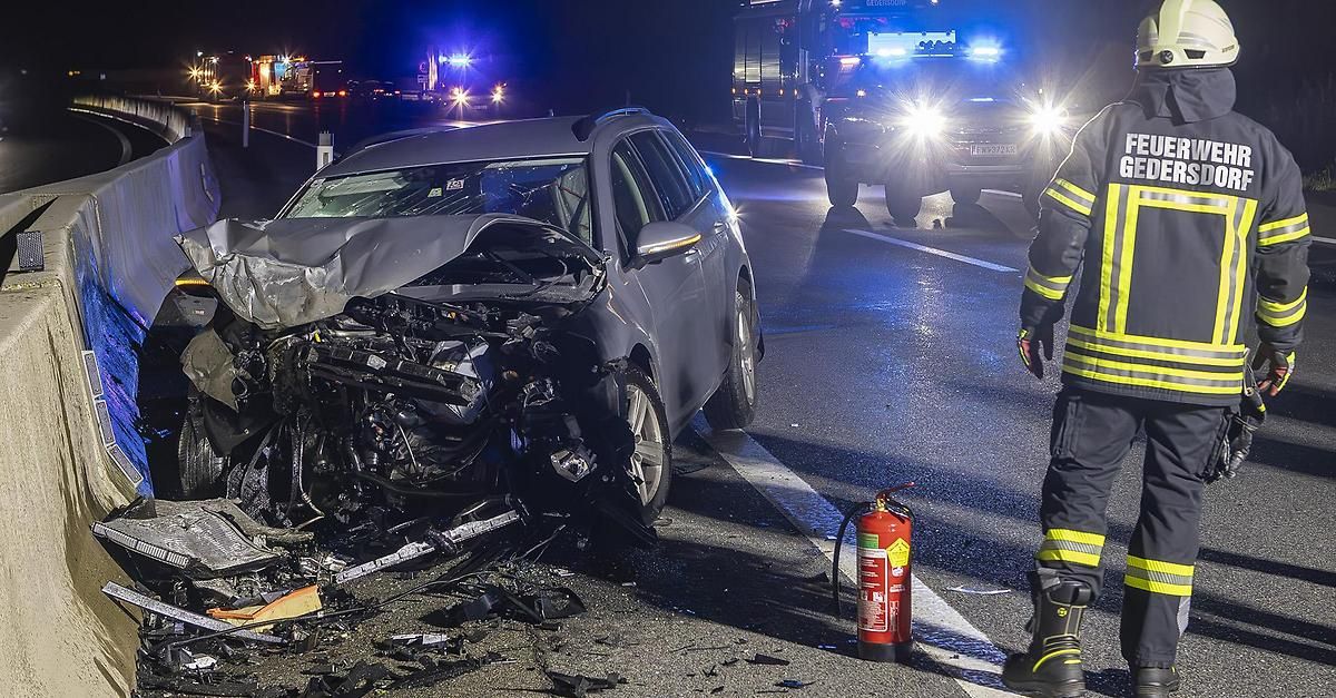 A car wrecked on the side of the road at night with emergency vehicles present.
