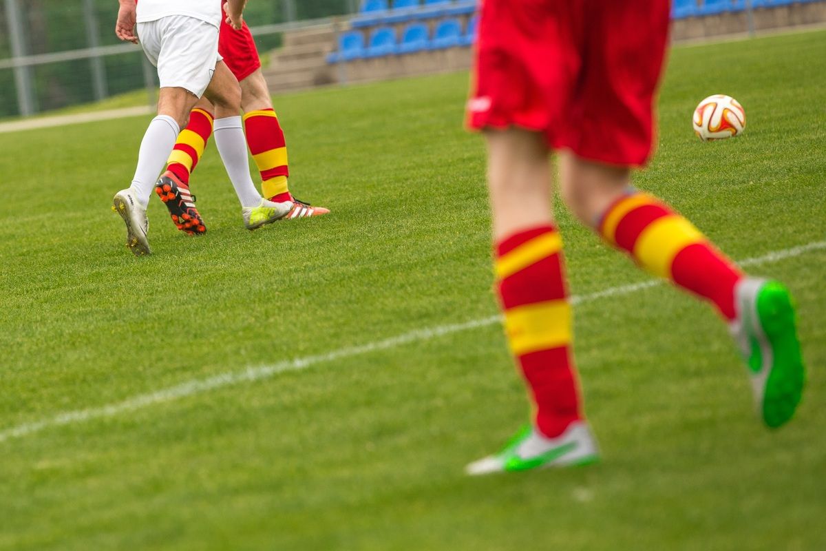 Soccer players in red and white uniforms are on a field with a white line. One player is blurry.