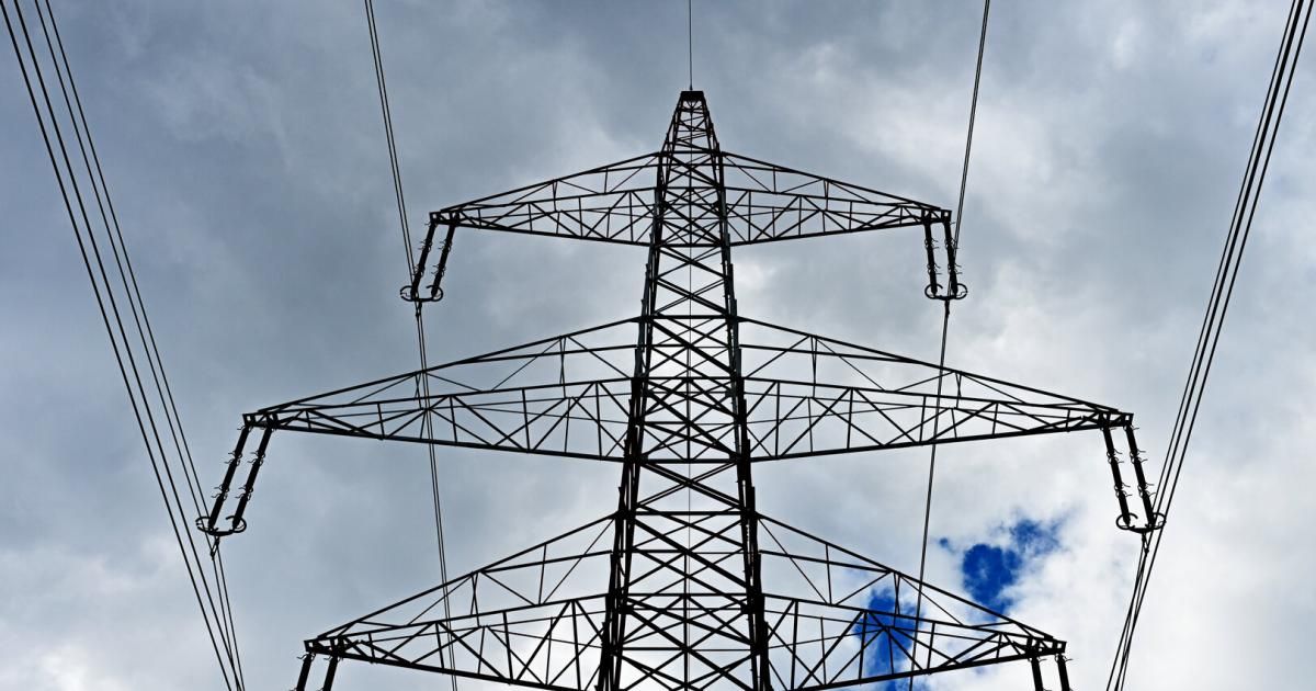 Ein hoher Stromleitungsmast mit mehreren Querverstrebungen und Kabeln vor einem bewölkten Himmel.