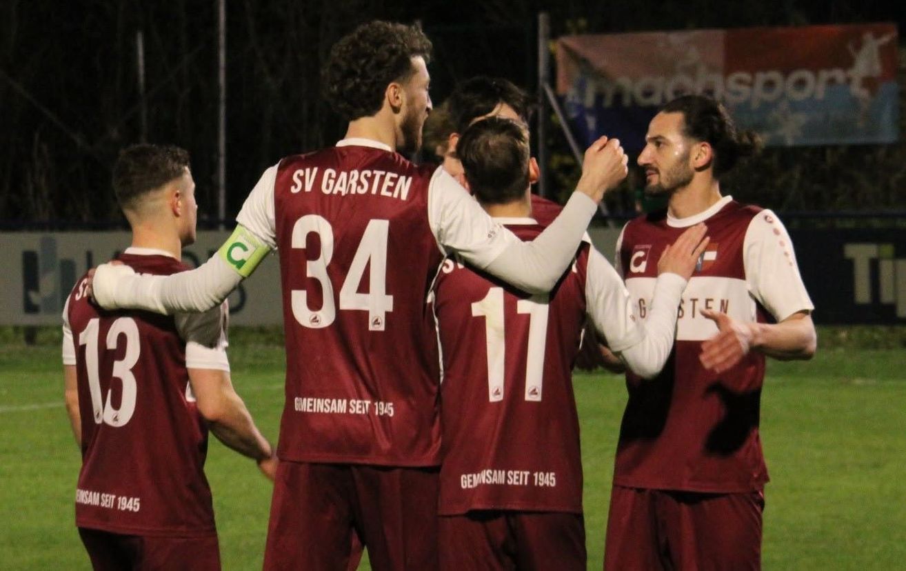 Eine Gruppe von Fußballspielern in braunen Trikots feiert auf dem Feld bei Nacht.