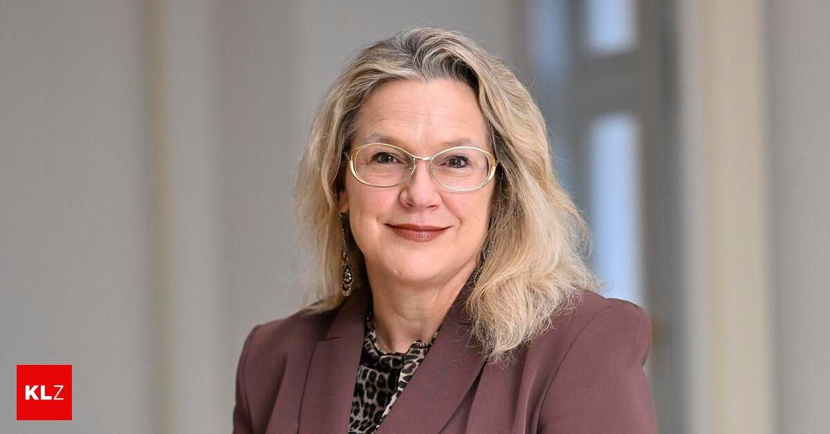 Eine Frau mit blonden Haaren, die eine Brille und einen kastanienbraunen Blazer trägt, posiert für ein Foto.