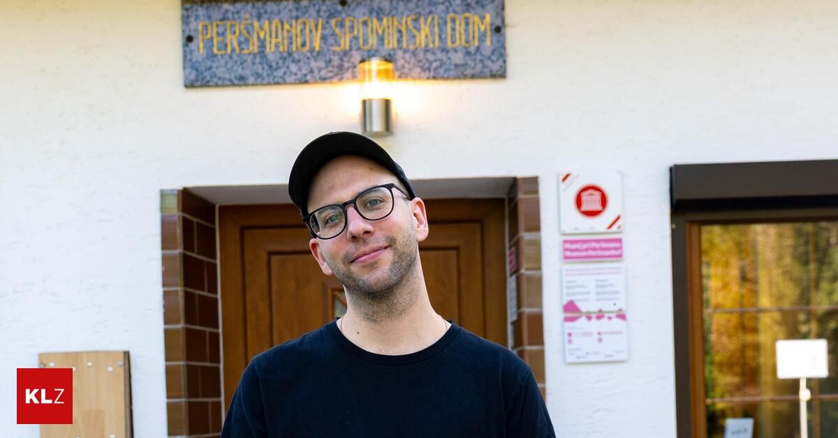 Ein Mann mit einer schwarzen Kappe und einer Brille steht vor einem Gebäude mit dem Schild 'Persmanov Spominski Dom'. Er lächelt und schaut in die Kamera.