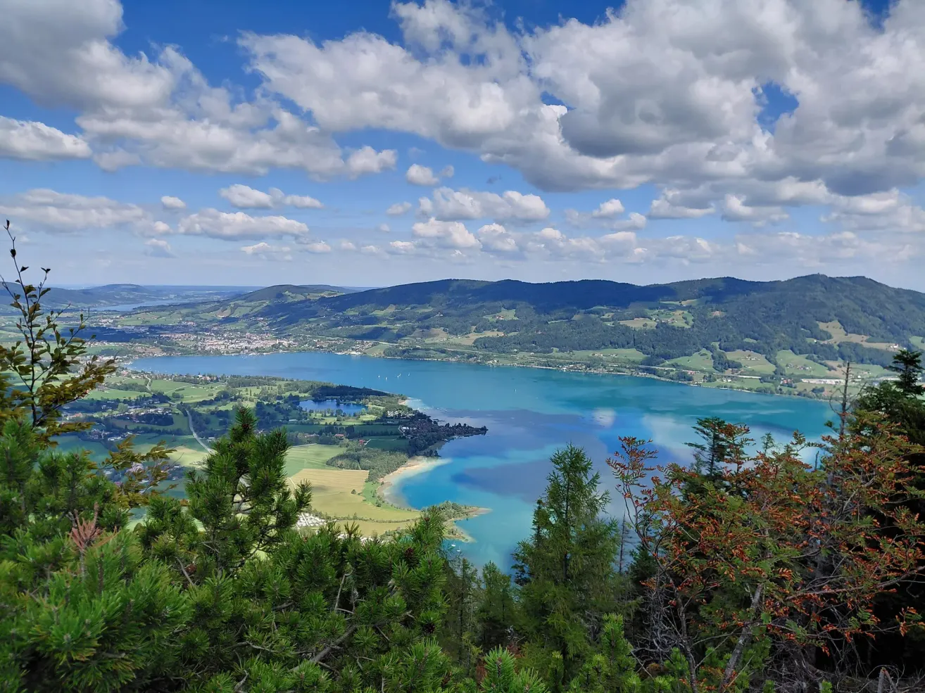 A panoramic view of a serene lake surrounded by lush green hills and a cloudy sky.