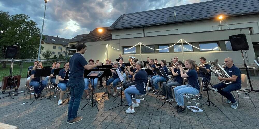 Ein Orchester spielt auf einer Bühne vor einem Gebäude mit Solarpanelen auf dem Dach.