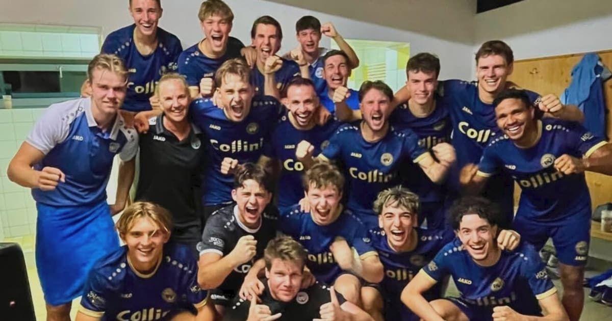 Eine Gruppe von Fußballspielern in blauen Trikots feiert einen Sieg, wobei ein Spieler in Schwarz im Vordergrund jubelt.