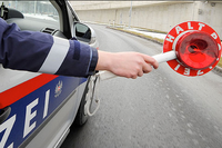Ein Polizist hält ein rotes Stoppschild vor einem Polizeiwagen auf der Straße.