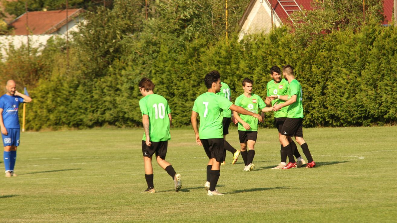 Fünf Fußballspieler in grünen Trikots laufen auf einem Feld, wahrscheinlich nach einem Spiel. Sie tragen alle schwarze Shorts und Socken.
