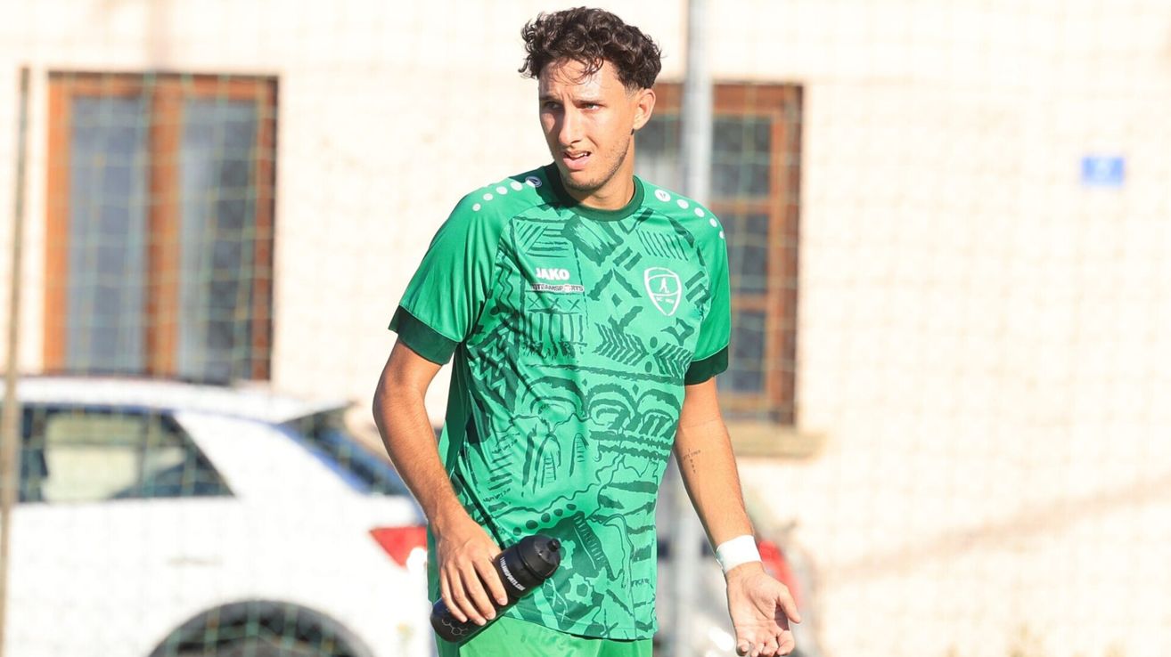 Ein Fußballspieler in einem grünen Trikot geht mit einer Wasserflasche und schaut nach vorne. Er trägt ein weißes Armband und hat eine Tätowierung am Arm.