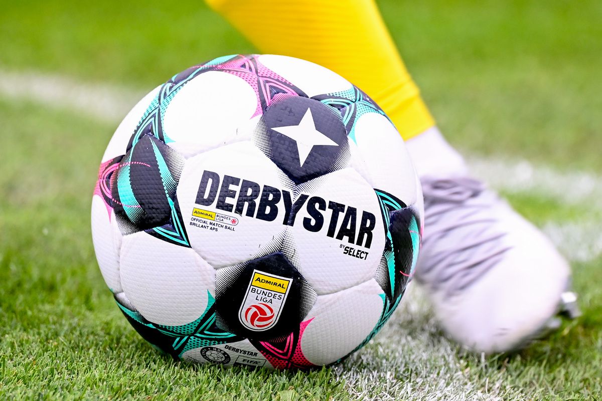 Nahaufnahme eines Derbystar-Fußballs mit einem weißen Stern und schwarzem Text auf einem Rasenfeld.