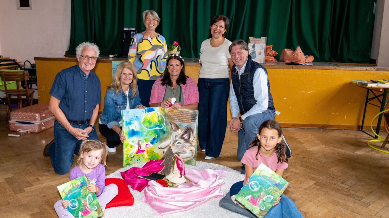 A group of adults and children are posing for a photo with a colorful painting and books on a table.