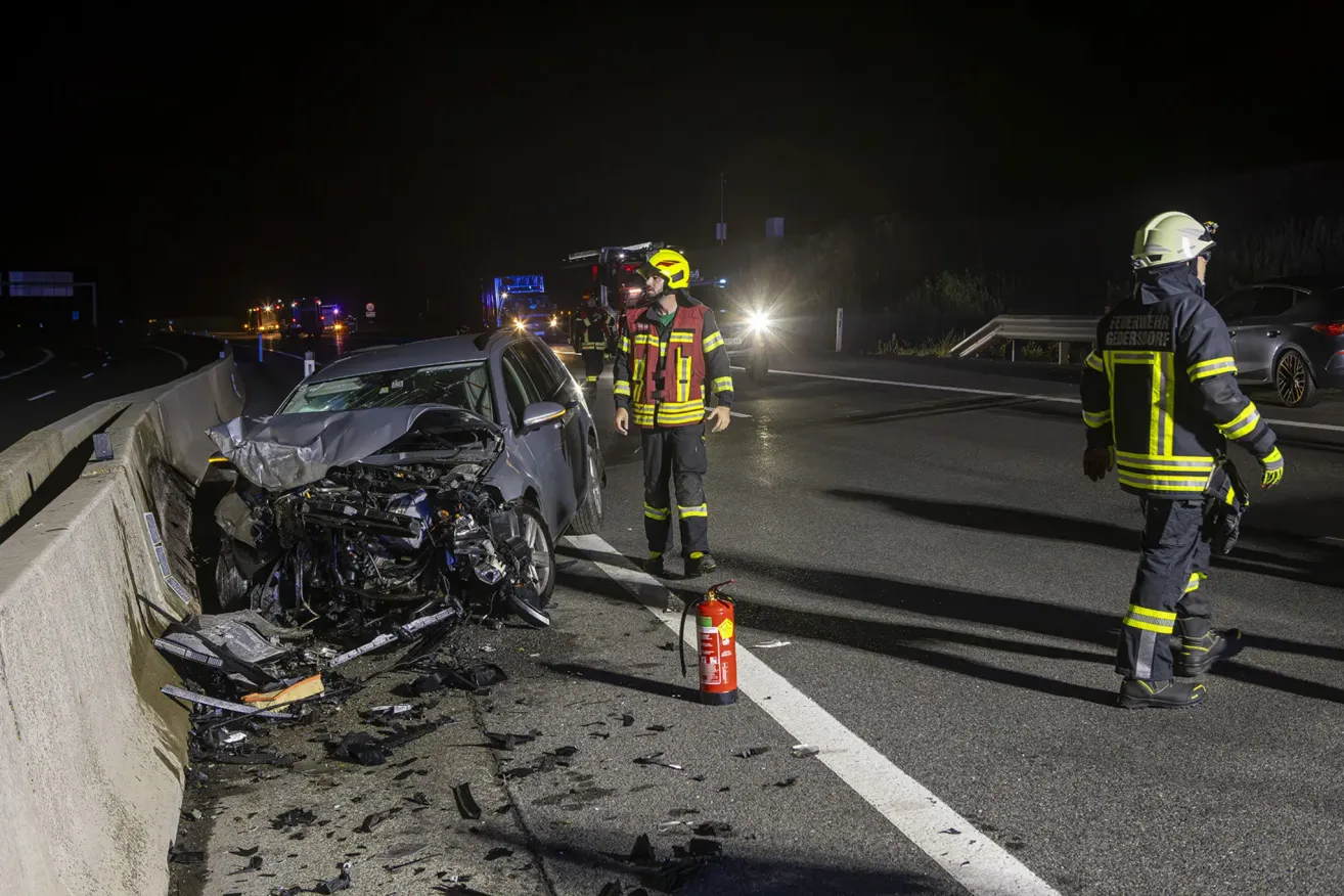 A firefighter in full gear walks past a wrecked car on the side of a road at night.
