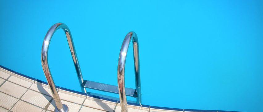 Ein leerer Swimmingpool mit einem Metallgeländer und einer gefliesten Kante. Das Wasser ist sauber und blau.